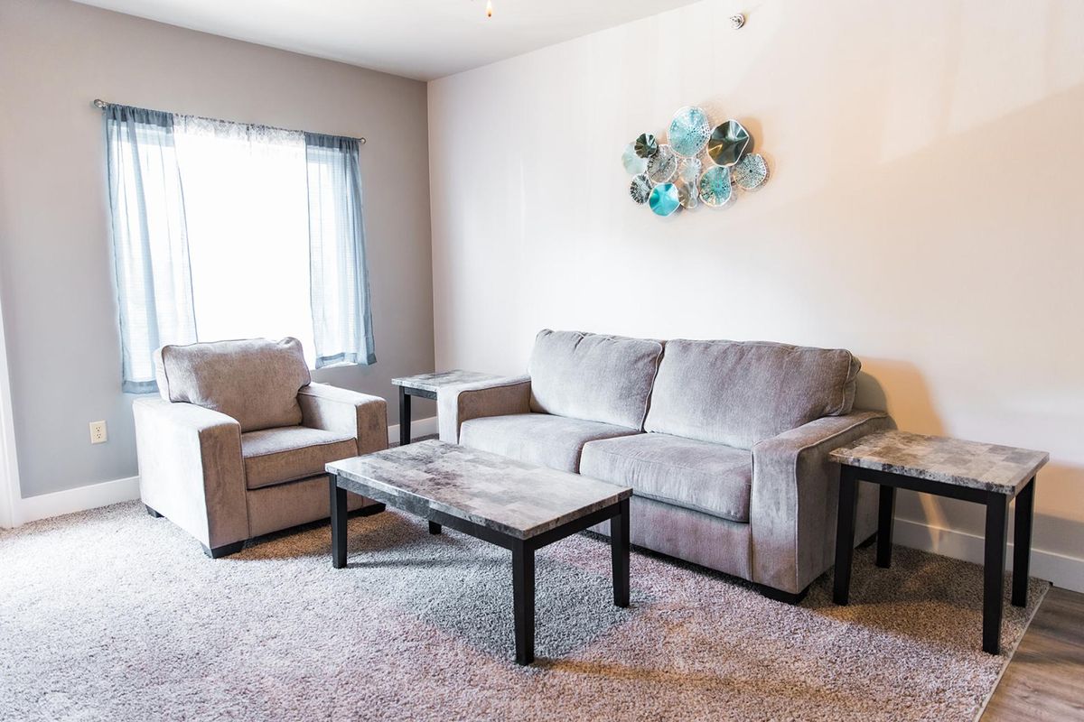 A cozy living room featuring a gray sofa, armchair, coffee table, and wall art.