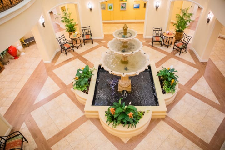 A decorative indoor lobby featuring a central fountain surrounded by seating and plants.