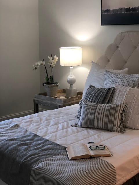 A cozy bedroom with a neatly made bed, an open book, and a lamp on the nightstand.