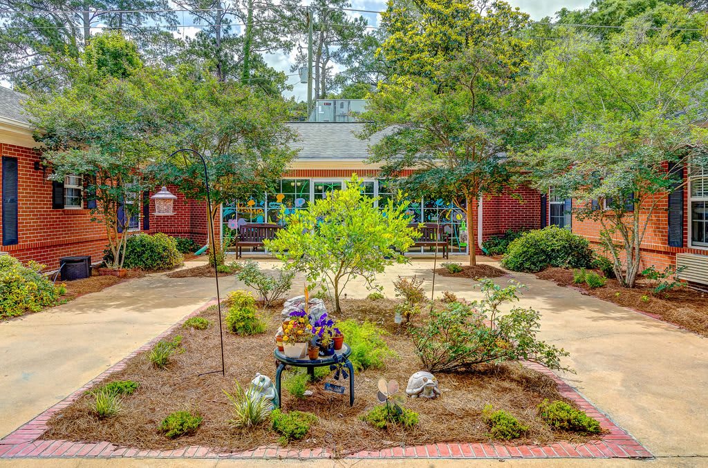 A peaceful garden scene with a sculpture on a bench and a building in the background.