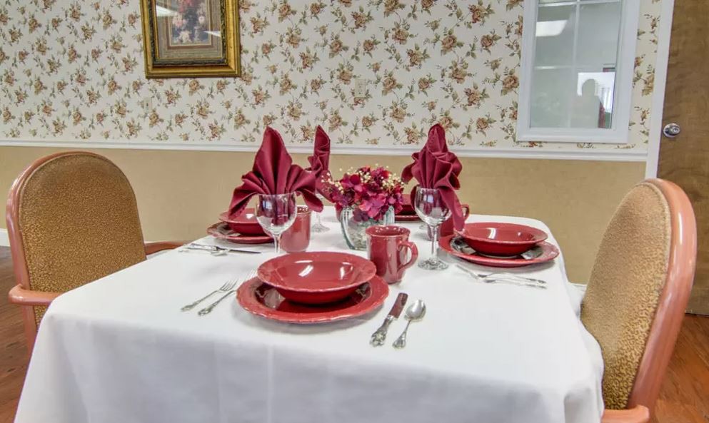 An elegantly set dining table with red dinnerware and folded napkins, accented by a floral centerpiece.