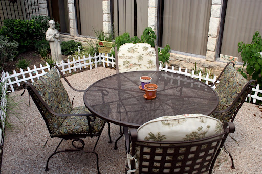 A cozy outdoor seating area featuring a round table and floral-patterned chairs, surrounded by greenery and decorative elements.