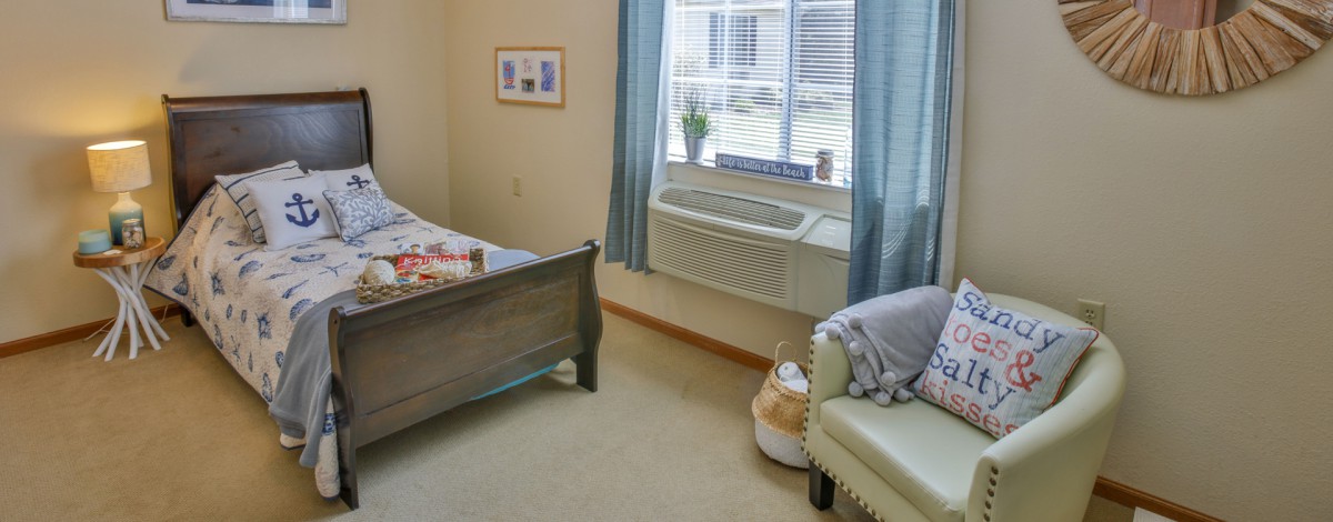 A cozy bedroom with a bed, armchair, and a window allowing natural light to fill the space.