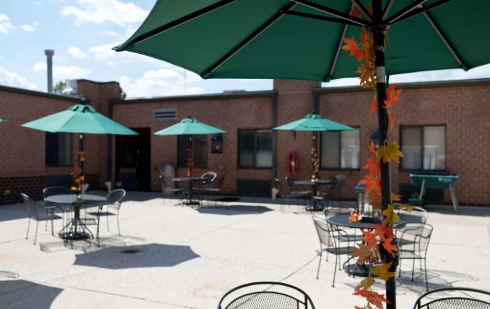 A sunny outdoor patio with tables, chairs, and umbrellas next to a brick building.