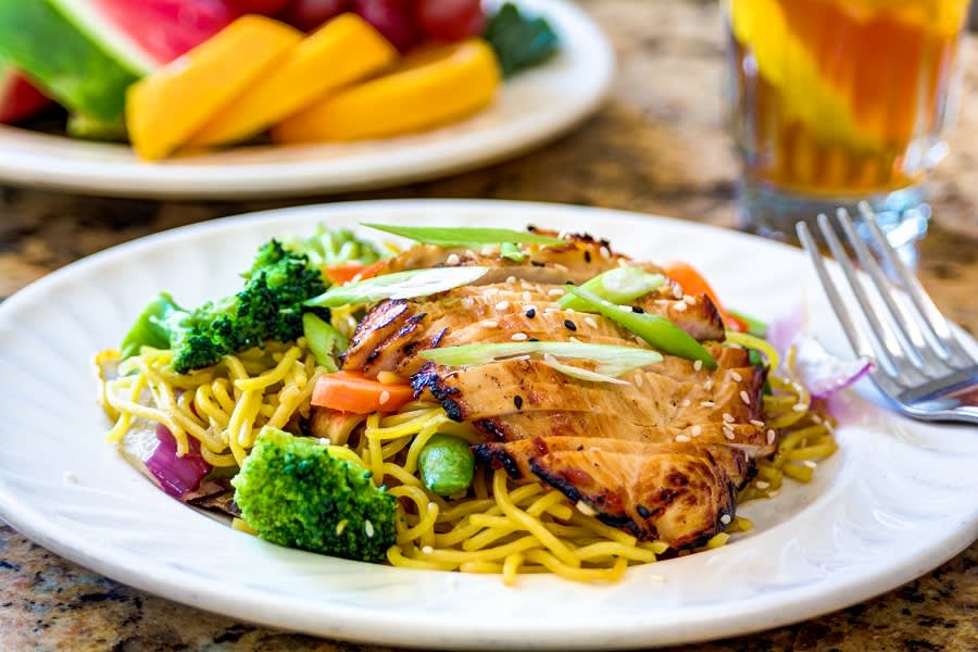 A delicious plate of noodles topped with grilled chicken and vegetables.