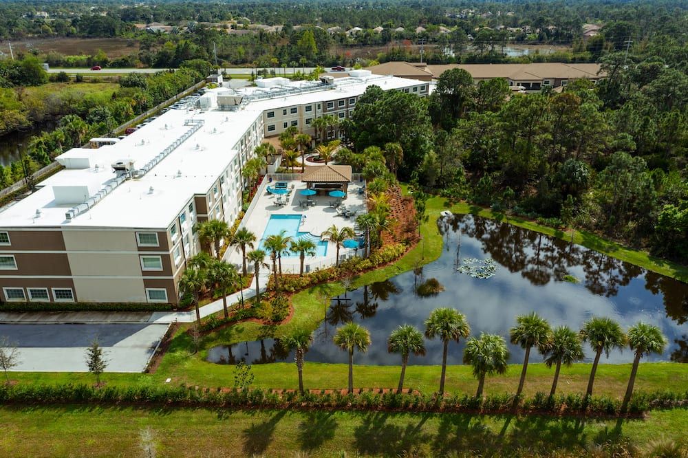 Aerial view of a hotel resort featuring a pool, surrounded by palm trees and a scenic pond.