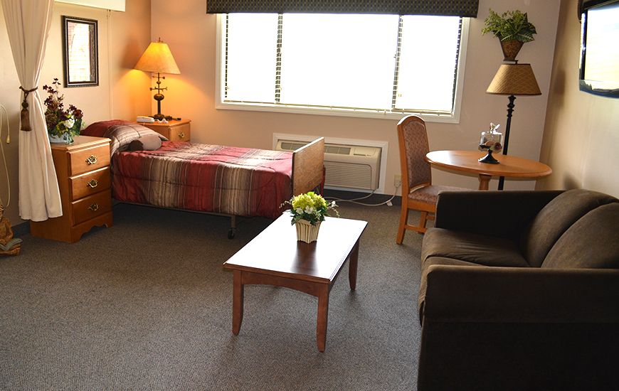 A cozy bedroom with a single bed, a sofa, a wooden coffee table, and a window.