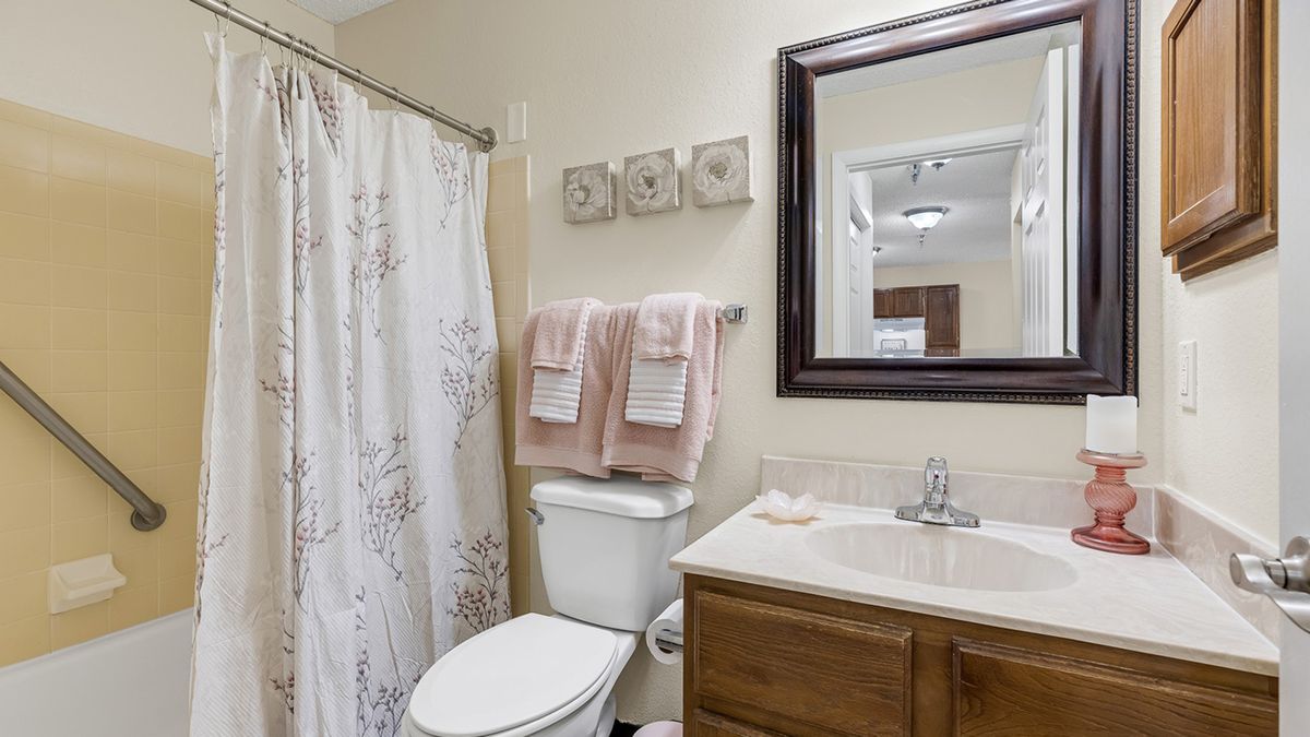 A well-organized bathroom featuring a sink with a mirror above, a toilet, and neatly arranged towels by the shower curtain.