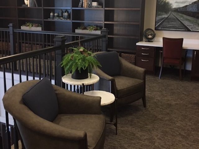 A comfortable office seating area with chairs, a plant on a side table, and shelves in the background.