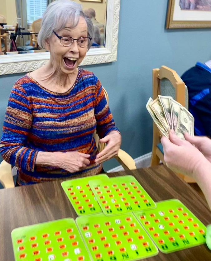 An elderly woman excitedly celebrates winning a bingo game with cash prizes.