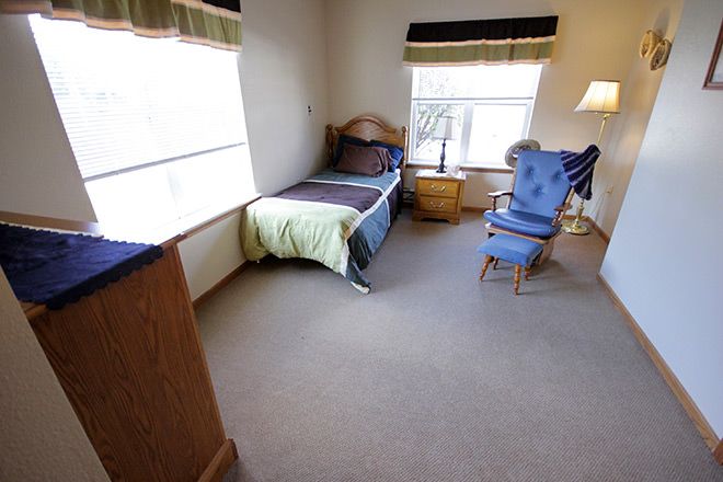 A cozy bedroom with a single bed, armchair, and wooden furniture.