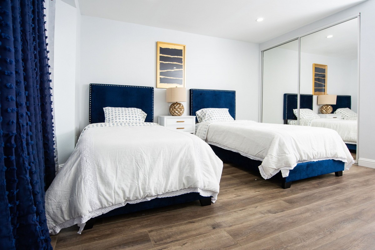 A neatly arranged bedroom featuring two twin beds with blue headboards and white bedding, complemented by a nightstand and modern decor.