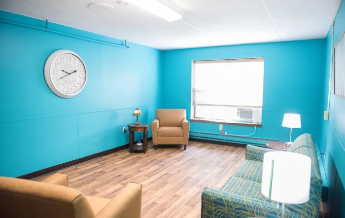A cozy living room with blue walls, featuring two armchairs and a window letting in natural light.