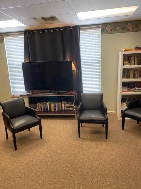 A cozy living room setup with three chairs, a television, and a bookshelf.