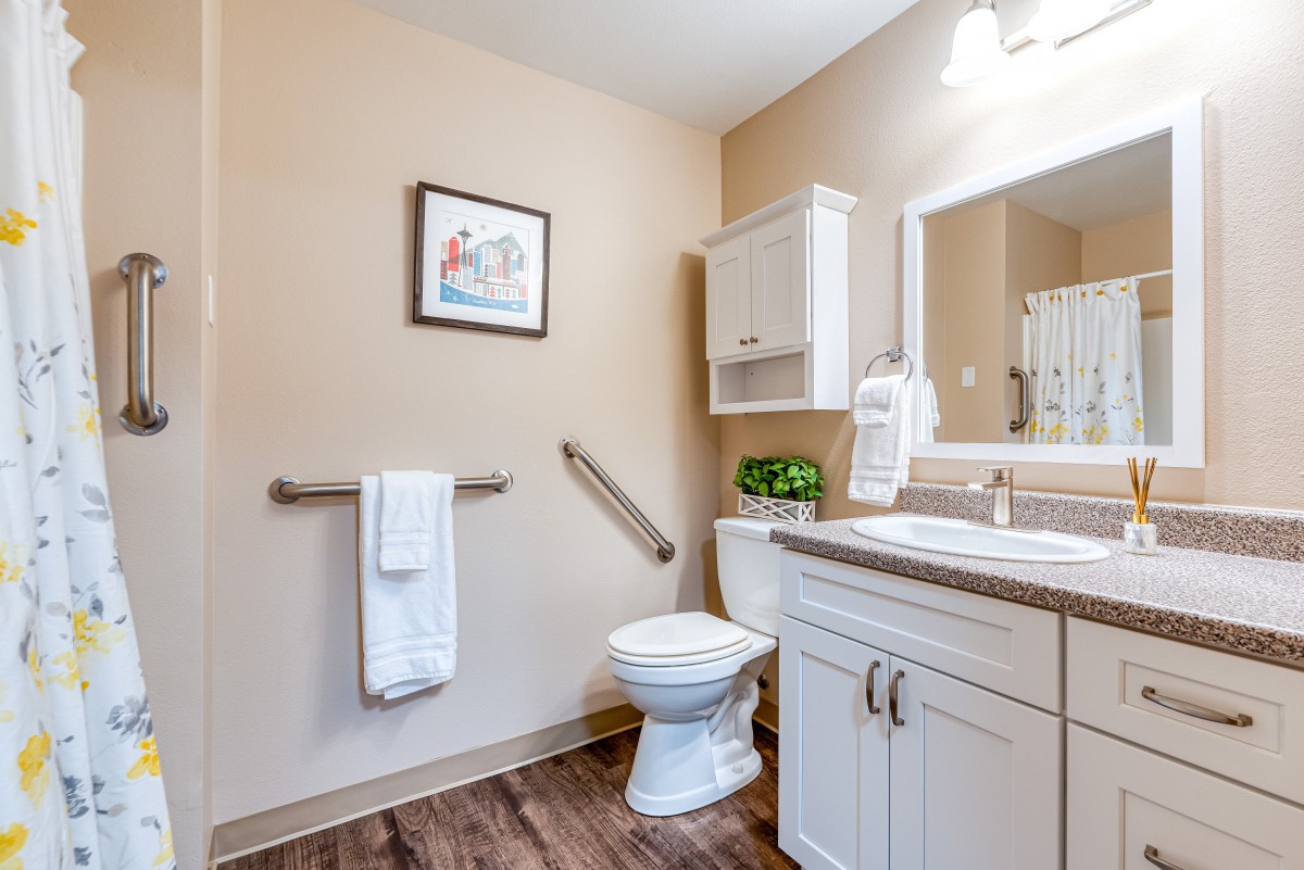 A neatly organized bathroom with a toilet, sink, mirror, and cabinet, featuring modern decor and a grab bar for safety.