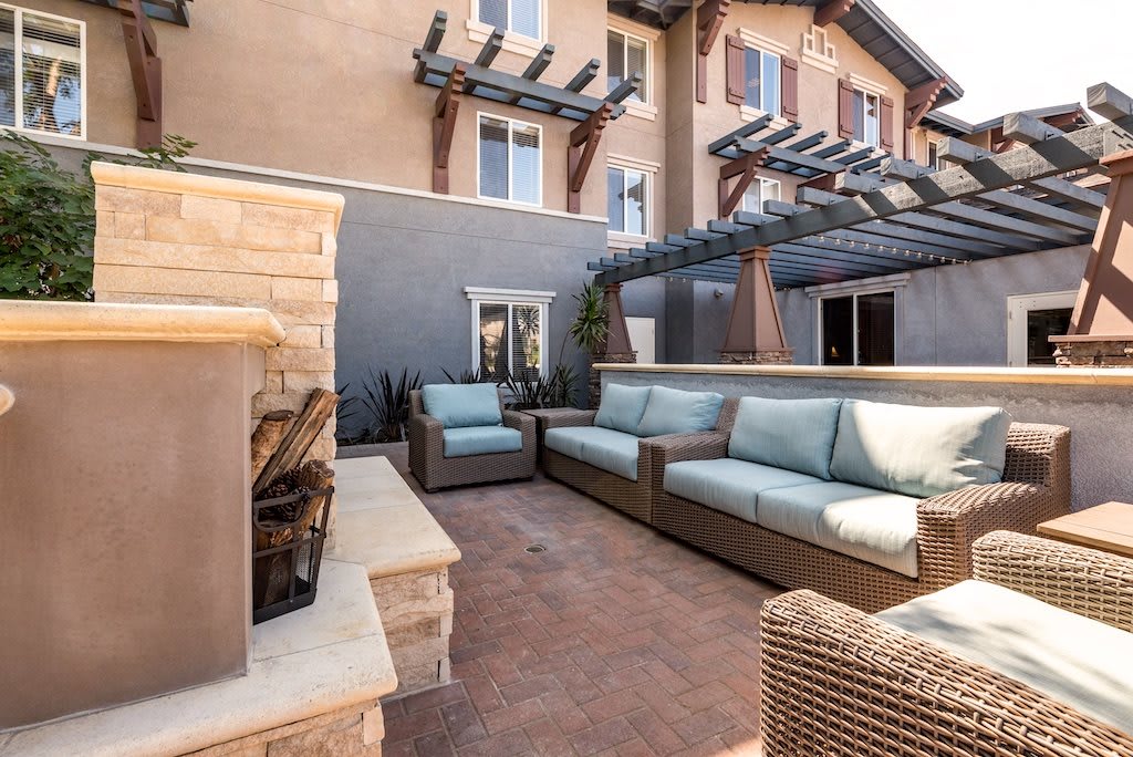 A cozy outdoor patio with comfortable sofas and a fireplace, set against a residential building.