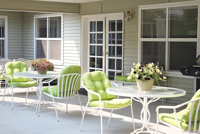 A cozy patio with green-cushioned chairs, tables, and vibrant flowers near French doors.