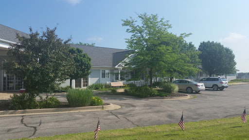 A sunny day view of a building surrounded by greenery and a parking area.