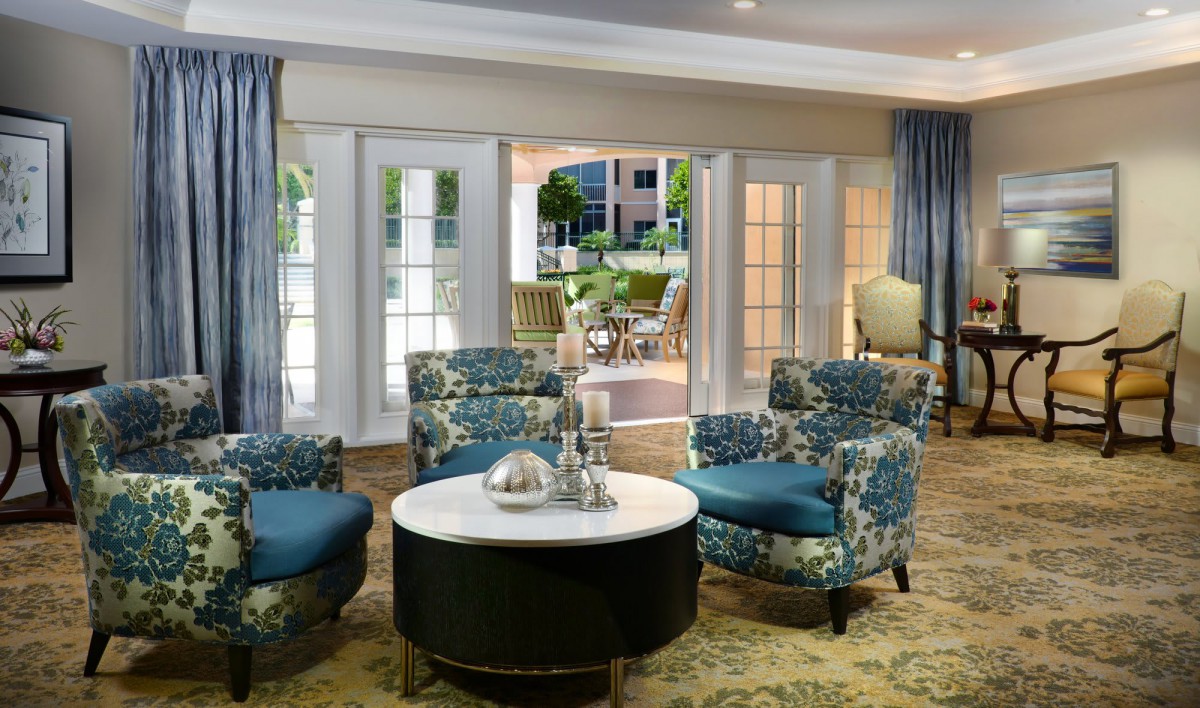 A stylishly decorated living room with floral armchairs and a round coffee table near large windows.