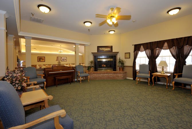 A cozy living room with a fireplace, armchairs, and a ceiling fan.