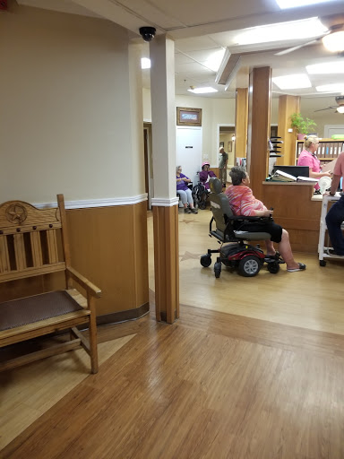 A view of a nursing home interior, showcasing the waiting area and residents using mobility aids.