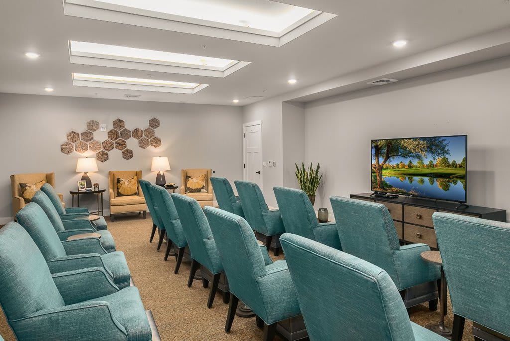 A modern conference room with rows of teal chairs facing a television.
