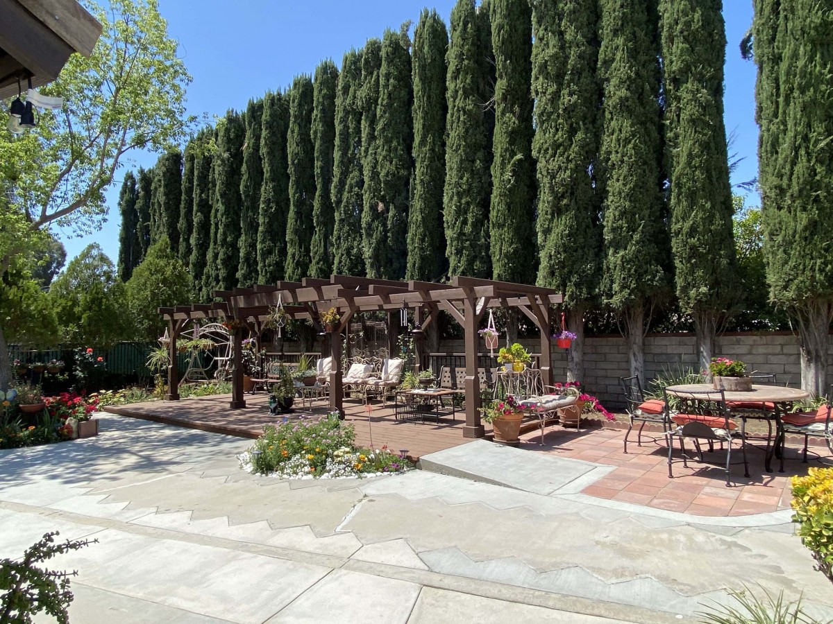A beautifully landscaped backyard featuring a pergola with outdoor seating and tall trees in the background.
