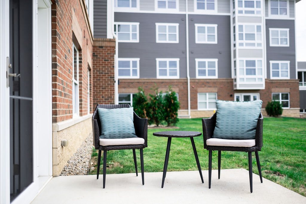 A cozy outdoor patio with two chairs and a side table in front of a modern apartment building.