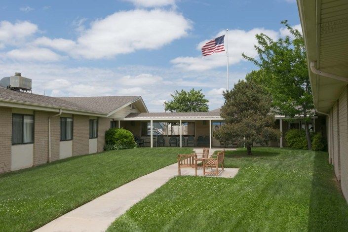 A building with a lush green lawn and outdoor seating, featuring an American flag in the background.
