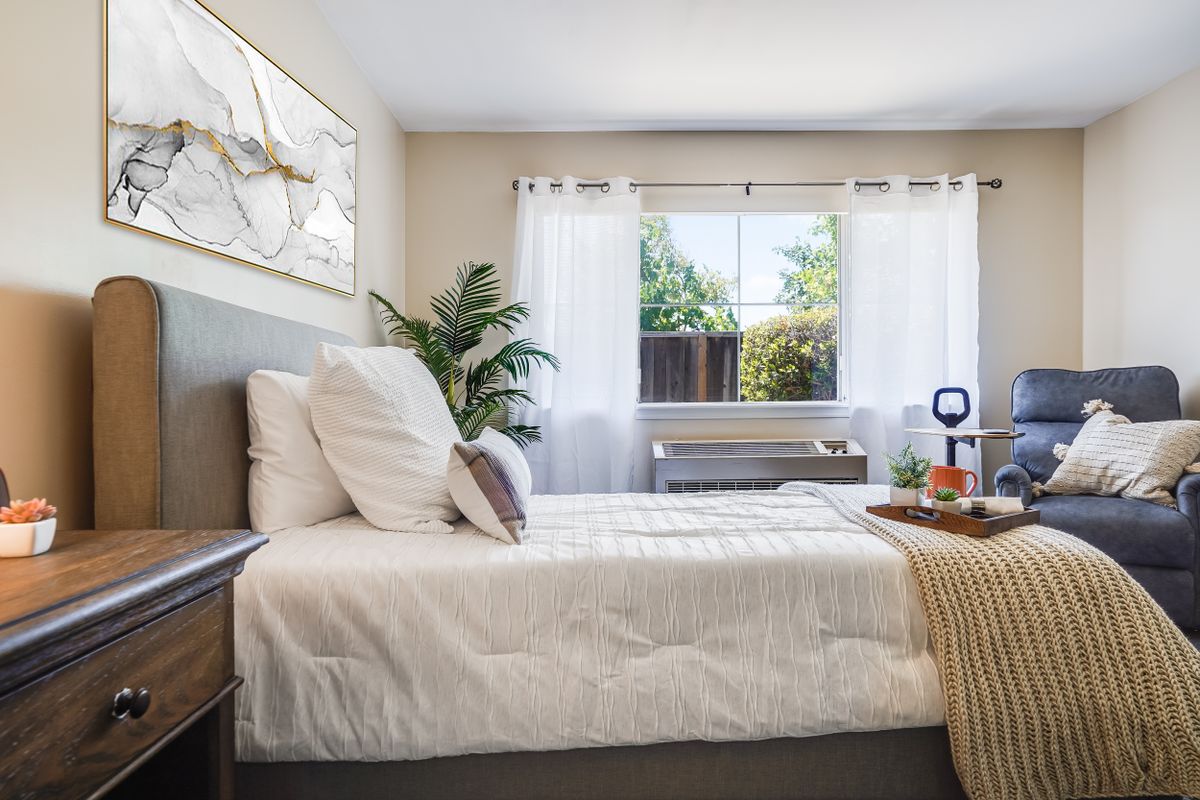 A bright and minimalist bedroom with a neatly made bed, large window, and stylish decor.