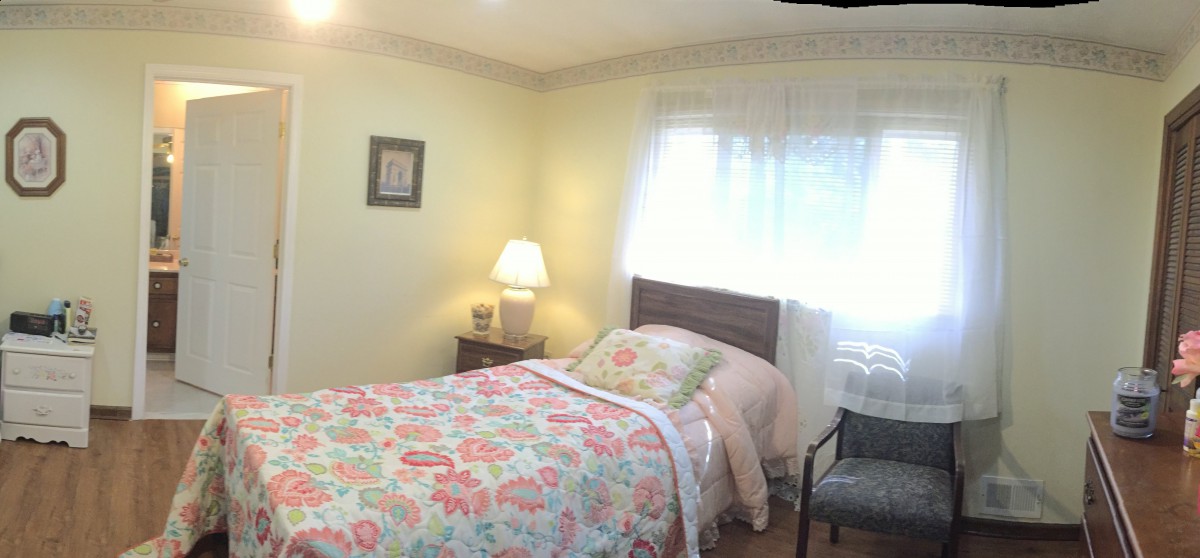 A cozy bedroom with a single bed covered in floral bedding, a bedside lamp, and a window letting in natural light.