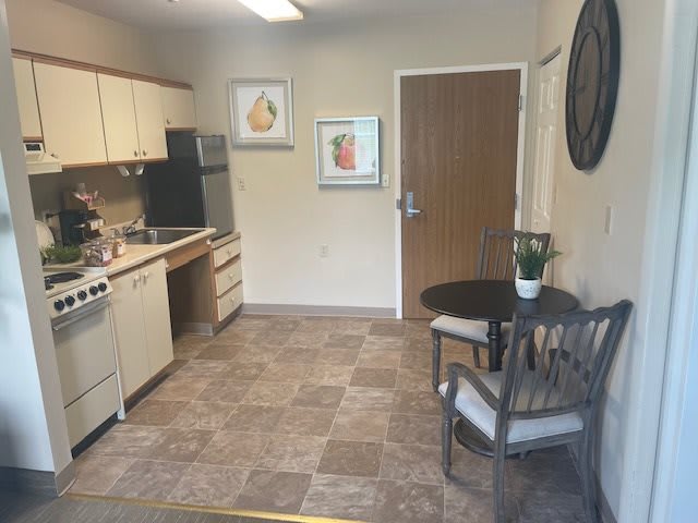 A cozy kitchen area with a small dining table and two chairs, featuring artwork on the walls and basic kitchen appliances.
