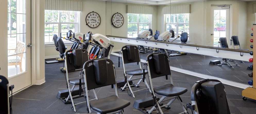 A fitness room equipped with exercise machines, chairs, and mirrors.