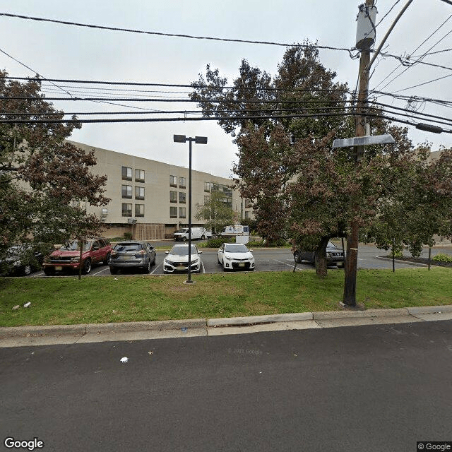A view of a building with a parking lot, cars, trees, and power lines along the street.