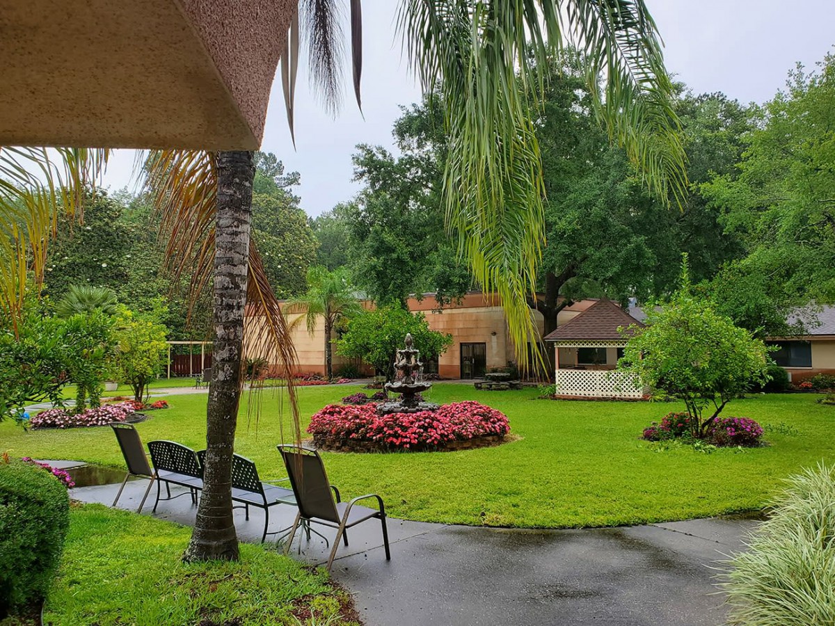 A serene garden with a central fountain, surrounded by lush greenery and garden chairs.