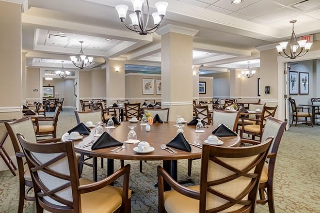 An elegantly set indoor dining room with neatly arranged tables and chairs, adorned with chandeliers.