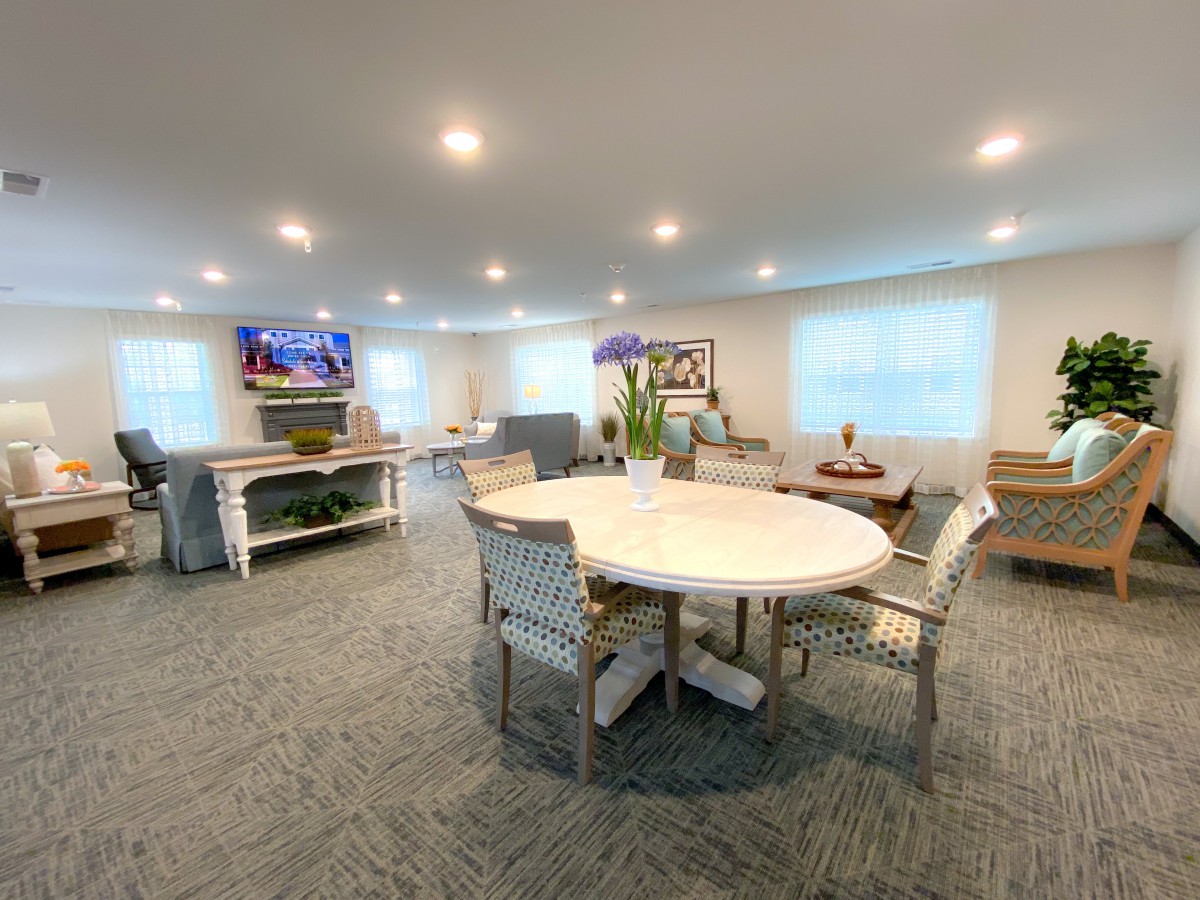 A cozy living room with modern furniture, featuring a round table and chairs, and a television mounted on the wall.