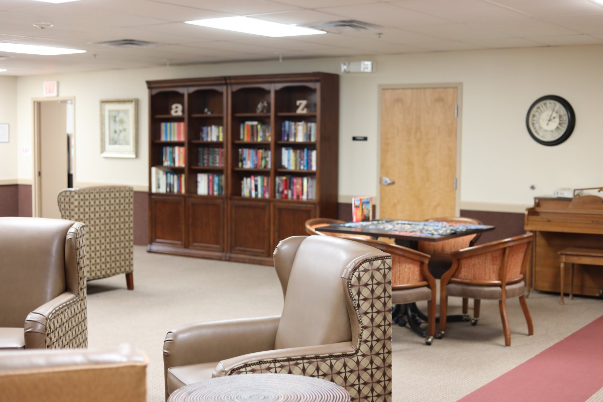 A cozy library space with bookshelves, comfortable seating, and a table.