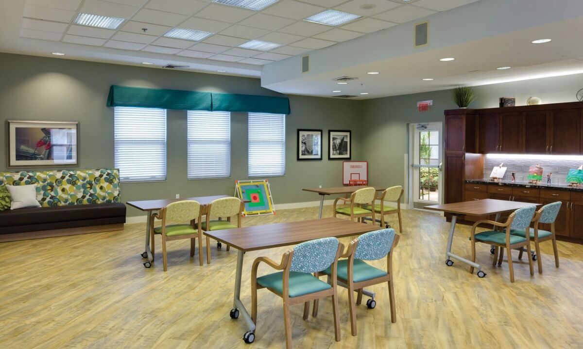 A well-lit dining room with multiple tables and chairs, featuring large windows and decorative wall art.