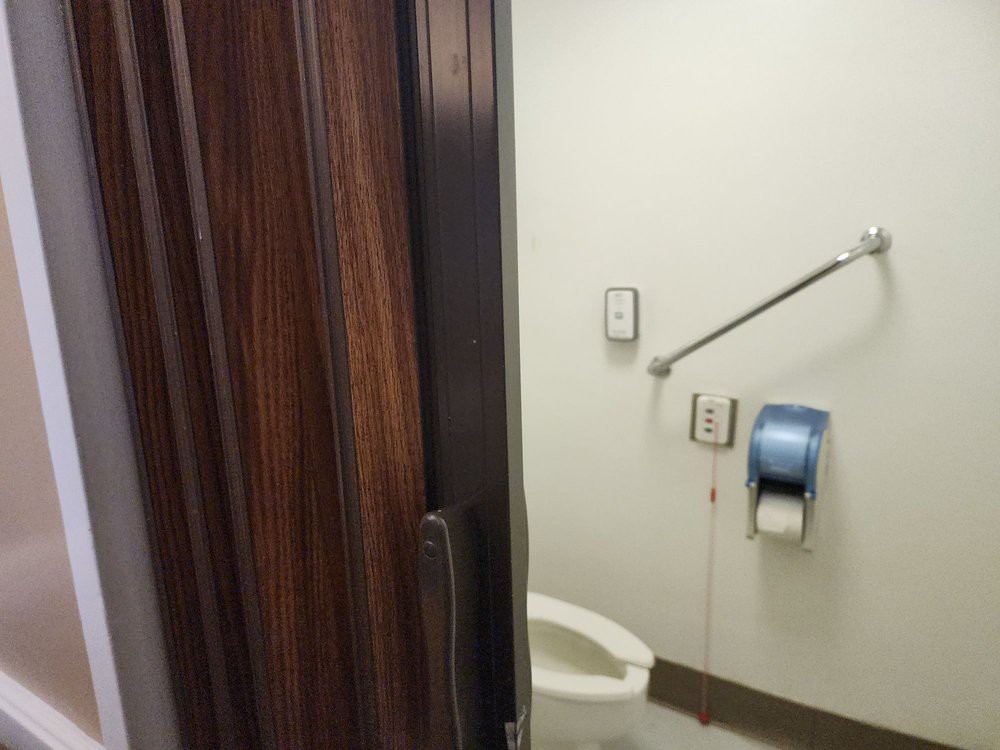 An open door of a public restroom stall revealing a toilet and toilet paper dispenser.