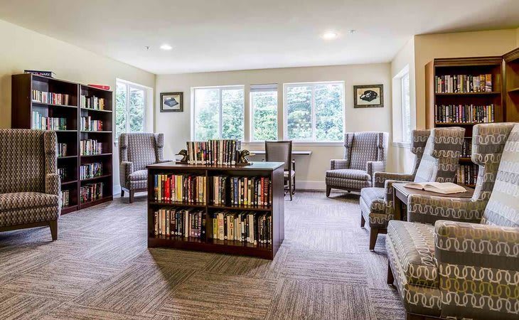 A cozy reading area with bookshelves, comfortable chairs, and large windows providing natural light.