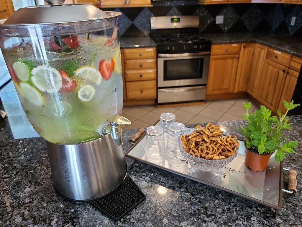 A kitchen countertop with a dispenser of infused water and a tray of snacks.
