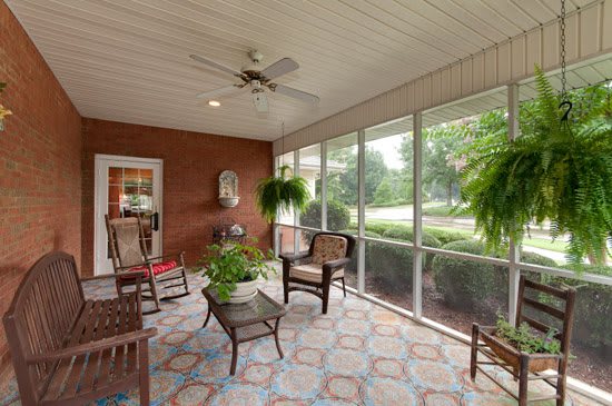 A cozy screened porch with comfortable seating, potted plants, and a ceiling fan.