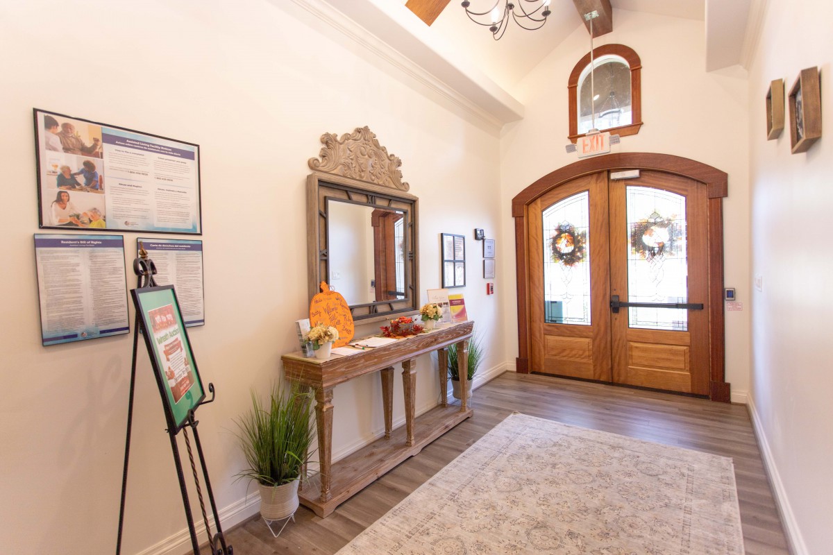 A welcoming entryway with a wooden door, decorative mirror, and potted plant.