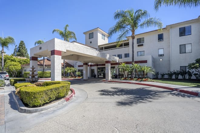 A building entrance with a driveway, surrounded by palm trees on a sunny day.