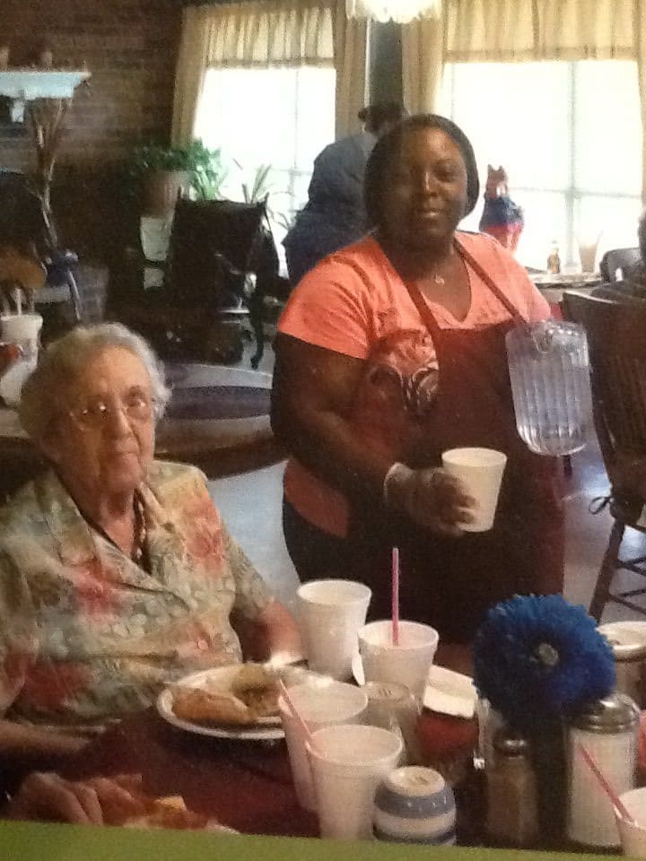 An elderly woman and a caregiver enjoying a meal at a dining area.