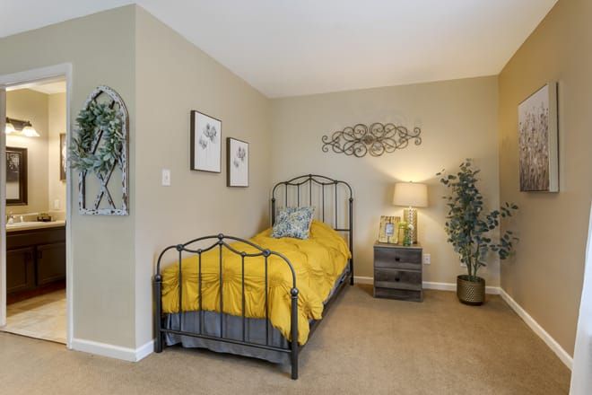 A cozy bedroom with a metal bed frame and bright yellow bedding, complemented by tasteful decor and greenery.