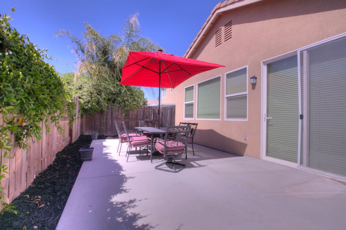 A sunny backyard patio with a table, chairs, and a red umbrella.