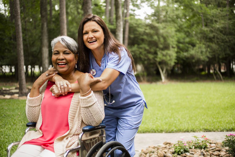 A nurse and an elderly woman in a wheelchair enjoy time outdoors together.