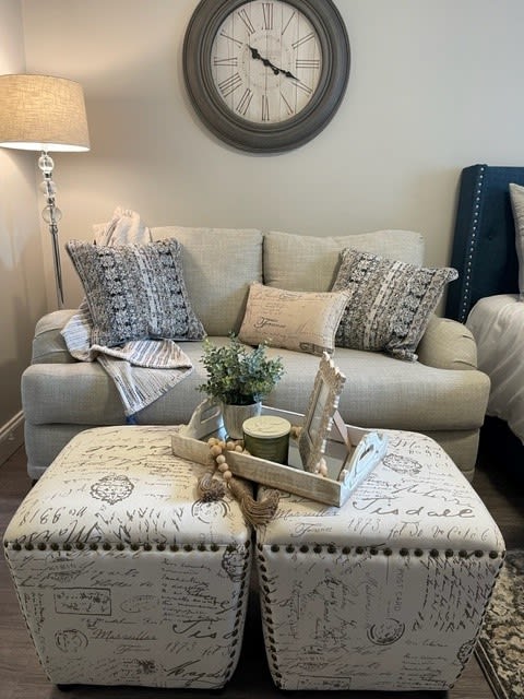 A cozy living room with a sofa adorned with decorative pillows, stylish ottomans, and a side lamp creating a warm ambiance.
